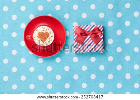 Cup of Cappuccino with heart shape symbol and gift box on polka dot background.