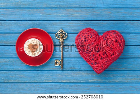 Cup of Cappuccino with heart shape symbol, key and toy on blue wooden background.