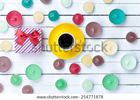 Cup of coffee with gift box and candles on white wooden background