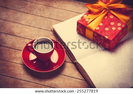 Cup of coffee and gift box with book on a wooden table. Photo in old color image style.