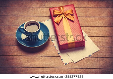 Cup of coffee and gift box with envelopes on a wooden table. Photo in old color image style.