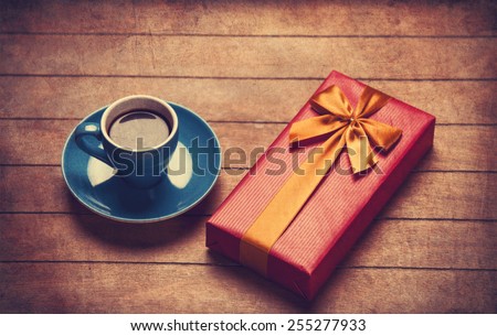 Cup of coffee and gift box on a wooden table. Photo in old color image style.