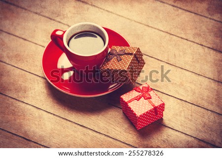 Cup of coffee and gift box on a wooden table. Photo in old color image style.