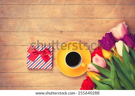 Cup of coffee and gift box near tulips on wooden background
