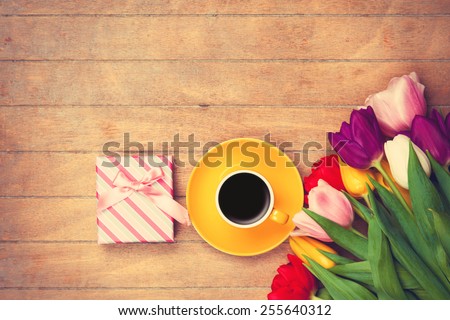 Cup of coffee and gift box near tulips on wooden background