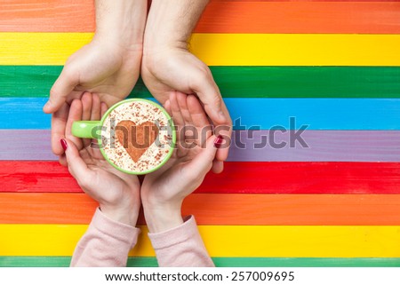Women and man holding cup of coffee with heart shape symbol on color background