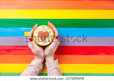 Female hands holding cup of coffee with heart shape on color background.