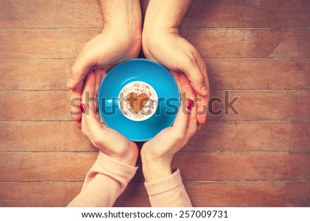 Women and man holding cup of coffee with heart shape symbol on a wooden background