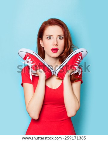 Surprised redhead girl in red dress with gumshoes on blue background.