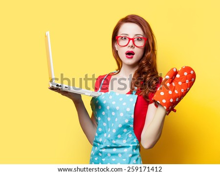 Surprised redhead housewife with oven gloves and computer on yellow background