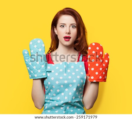 Redhead girl with oven gloves and apron on yellow background