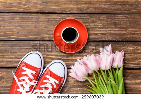 Gumshoes with coffee and tulips on a wooden background.