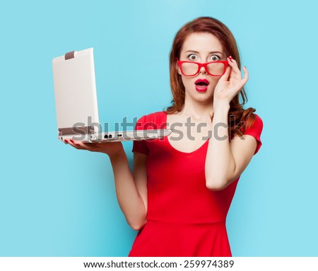 Surprised redhead girl with laptop on blue background