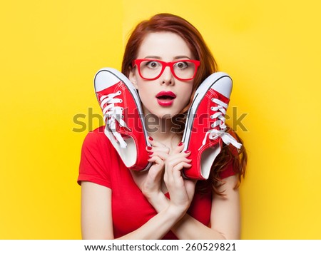 Surprised redhead girl in red dress with gumshoes on yellow background.
