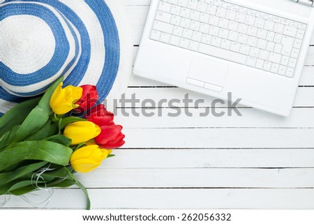 White computer and bouquet of tulips on white wooden background