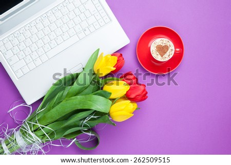 Cup of cappuccino with heart shape and computer, tulips on violet background.