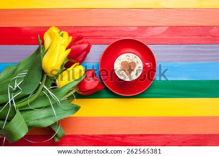 Cup of cappuccino with heart shape and bouquet of tulips on multicolor background.