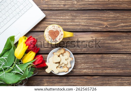 Cup of cappuccino with heart shape and computer, tulips on wooden background.