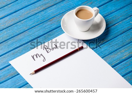 pencil and paper with inscription r cup of coffee on blue wooden table