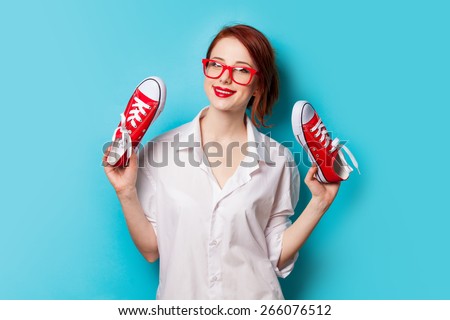 Beautiful redhead girl in white shirt with gumshoes on blue background.
