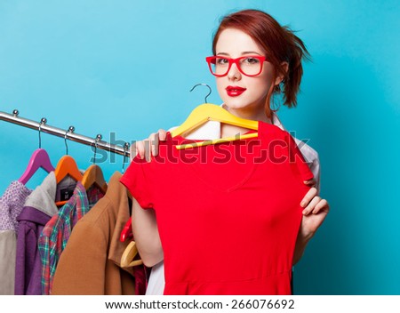 Young redhead designer with red dress and clothes on blue background