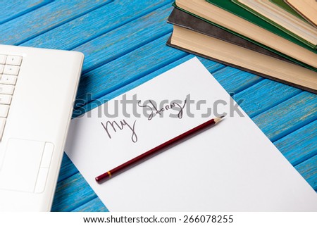pencil and paper with My Story words near notebook on blue wooden table