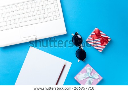 Computer and paper with sunglasses and gift boxes on blue background