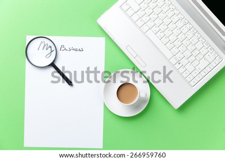 loupe, paper and cappuccino with computer on green background