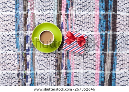 Cup of cappuccino with gift box on carpet background. Above view