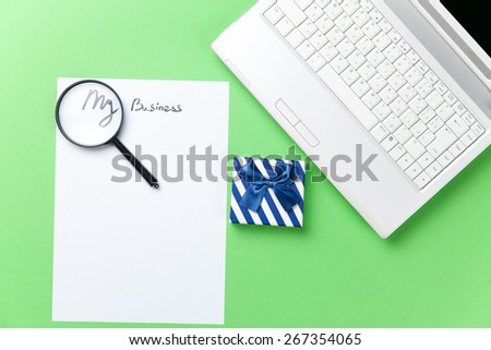 loupe, paper and gift with computer on green background