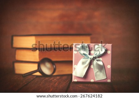 Books with loupe and gift box on wooden background.