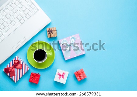 Cup of coffee with gift boxes and computer on blue background