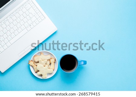Cup of coffee and cookies with notebook on blue background