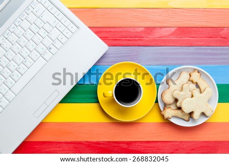 Cup of coffee with cookies and laptop on multicolored background