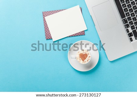 Cup of cappuccino with heart shape and laptop with mail on blue background.