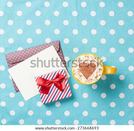 Cup of cappuccino with heart shape and envelope with gift box on blue polka dot background.