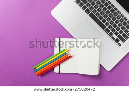 Note with laptop and pencils on violet background. View above