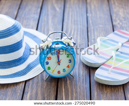 Alarm clock and hat with flip flops on wooden table.