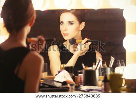 Portrait of a beautiful woman as applying makeup near a mirror. Photo in retro color style.