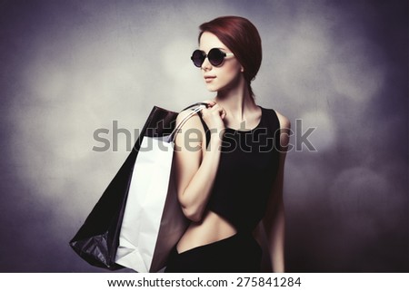 Style redhead girl with sunglasses and black dress with shopping bags on grey background