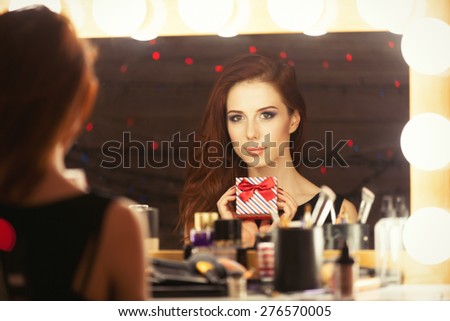 Portrait of a beautiful woman with gift box near a makeup artist mirror. Photo in retro color style.