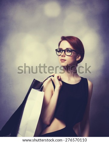 Style redhead girl with glasses and black dress with shopping bags on grey background