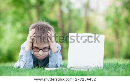 young sad boy with laptop computer on green grass in the park