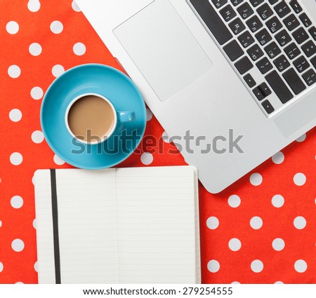 Cup of coffee and notebook near laptop comuter on red polka dot background