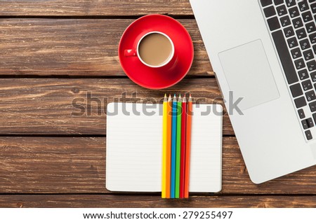 Cup of coffee and paper with laptop computer and color pencils on wooden background