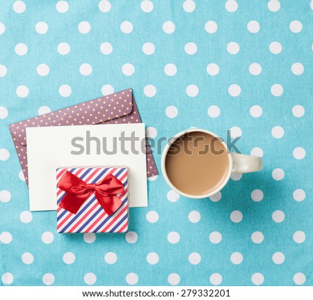 Cup of coffee and envelope with gift boxes on blue polka dot background
