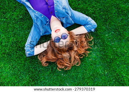 Beautiful redhead women lying down on green grass in summer time in the park.