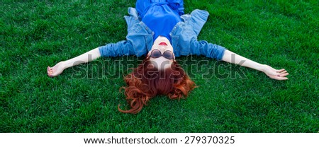 Beautiful redhead women lying down on green grass in summer time in the park.