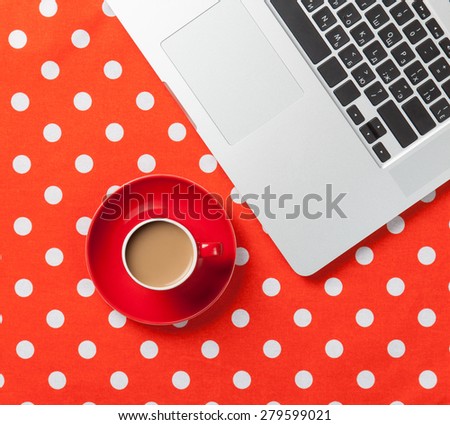 Cup of coffee and laptop computer on red polka dot background