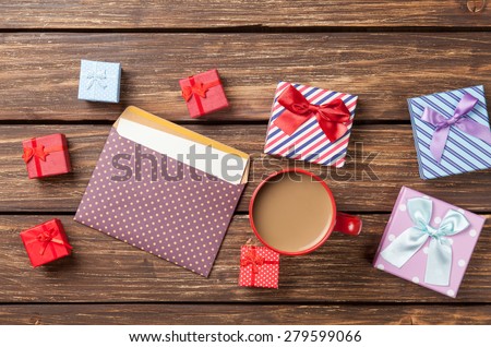 Cup of coffee and envelope with gift boxes on wooden table